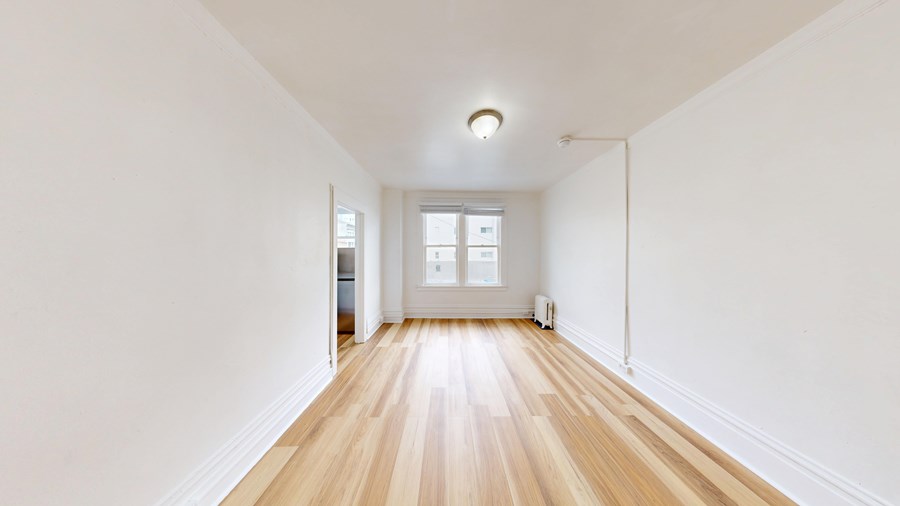 A long, empty room with wooden floors and white walls.